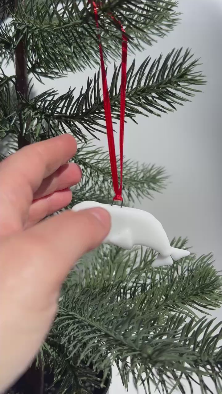 Béluga en verre fait main avec ruban rouge dans branches de sapin